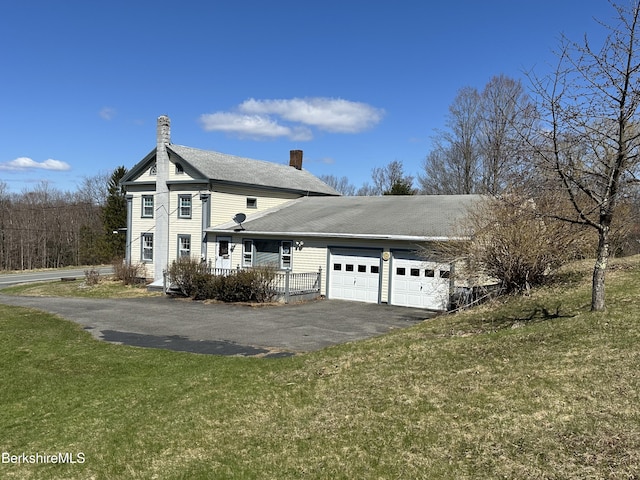 view of property exterior with a chimney, driveway, an attached garage, and a yard