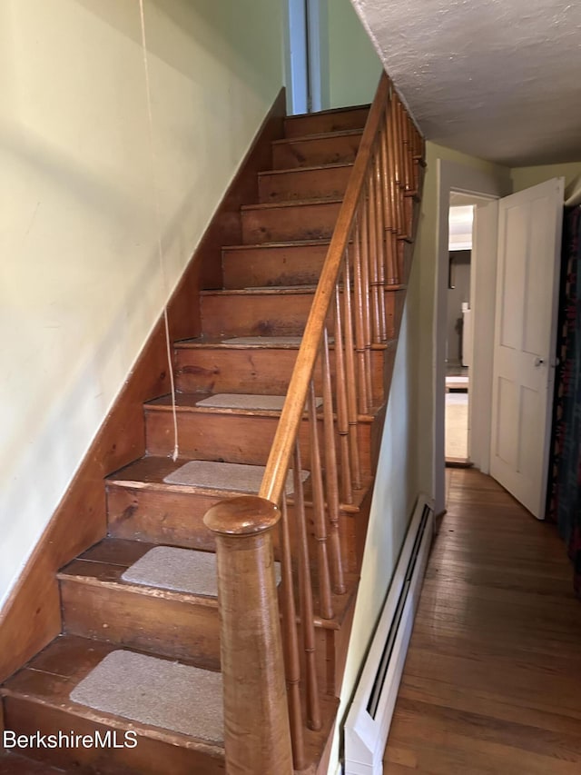 stairway with baseboard heating and wood finished floors