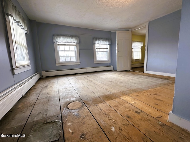 spare room featuring a baseboard radiator, hardwood / wood-style flooring, baseboards, and a textured ceiling