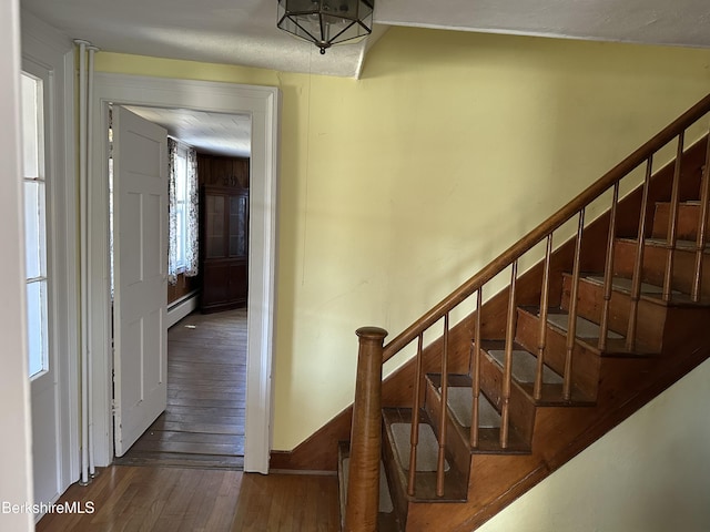 stairway featuring hardwood / wood-style flooring, baseboard heating, and baseboards