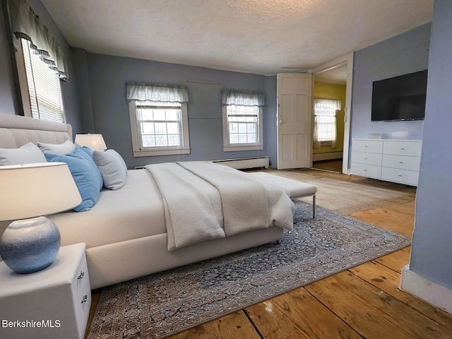 bedroom with a baseboard heating unit, hardwood / wood-style floors, and a textured ceiling