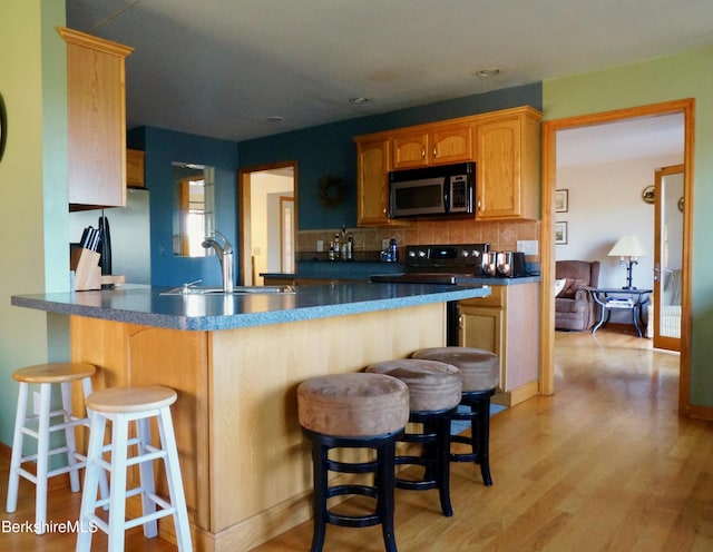 kitchen with kitchen peninsula, a kitchen bar, backsplash, sink, and light hardwood / wood-style floors