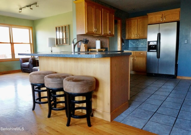 kitchen with sink, tasteful backsplash, stainless steel fridge with ice dispenser, kitchen peninsula, and a breakfast bar