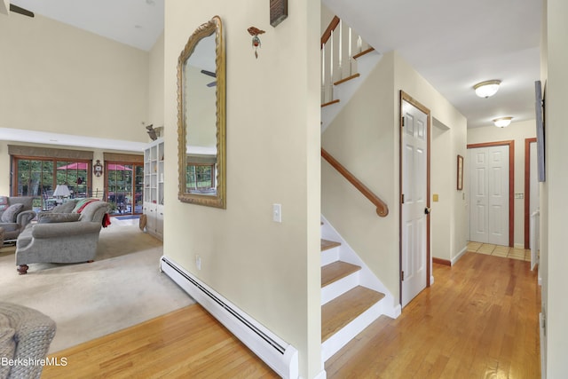 stairway featuring hardwood / wood-style flooring, a baseboard heating unit, and a towering ceiling