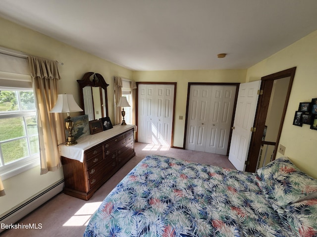 bedroom with baseboard heating, light colored carpet, and two closets