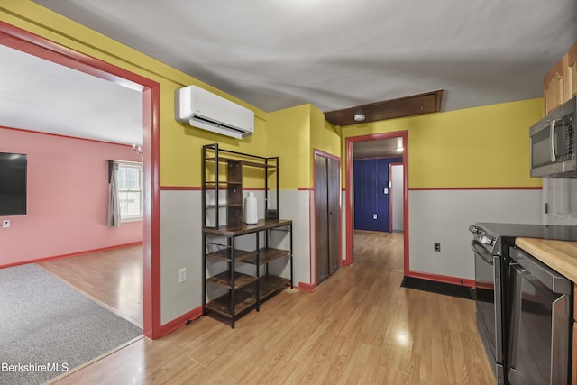 kitchen featuring a wall unit AC, light wood-style flooring, appliances with stainless steel finishes, and baseboards