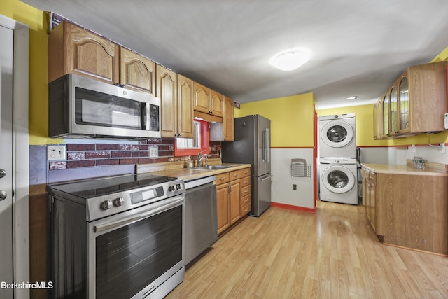 kitchen featuring glass insert cabinets, stacked washer / drying machine, stainless steel appliances, light wood-type flooring, and a sink