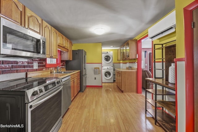 kitchen with a wall unit AC, appliances with stainless steel finishes, stacked washer / drying machine, light countertops, and light wood-type flooring