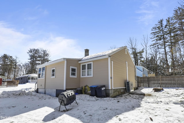 snow covered back of property with central air condition unit, a chimney, and fence