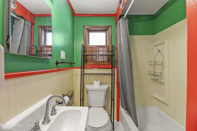 full bath with toilet, shower / bath combo with shower curtain, a sink, and wainscoting