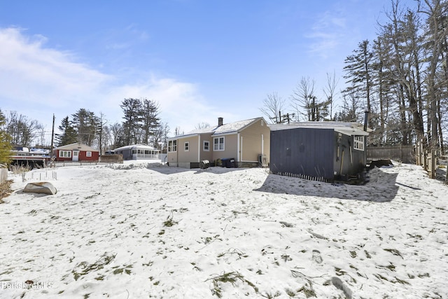 snow covered property featuring an outbuilding, a shed, and fence