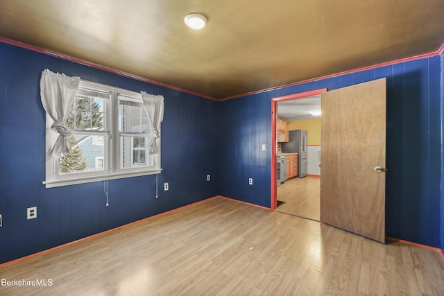 unfurnished bedroom with ornamental molding, freestanding refrigerator, and wood finished floors