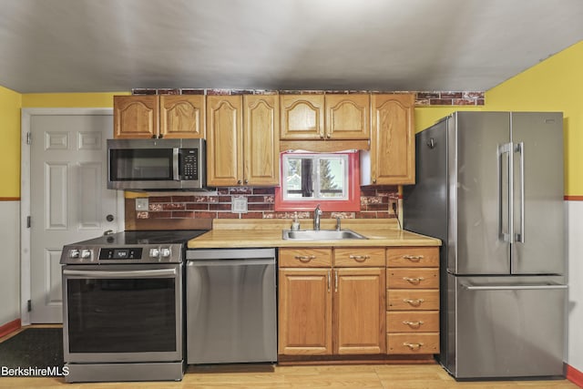 kitchen featuring tasteful backsplash, appliances with stainless steel finishes, light countertops, light wood-style floors, and a sink