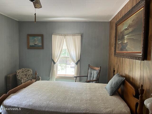 bedroom with ceiling fan, wood walls, ornamental molding, and radiator