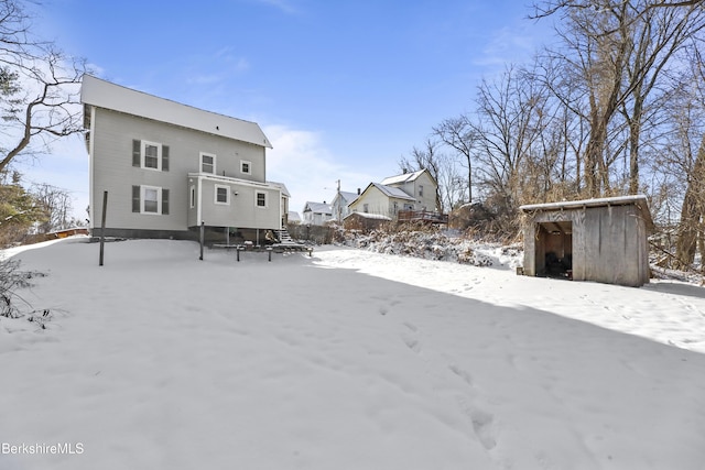 snow covered back of property featuring a storage shed