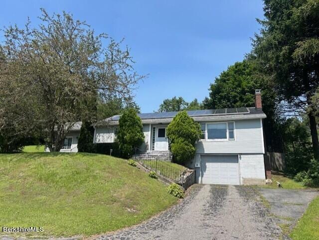 view of front of house with a garage, a front yard, and solar panels