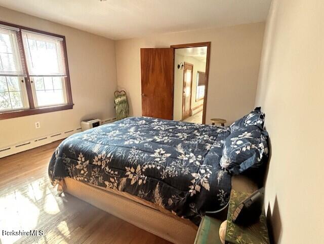 bedroom featuring a baseboard heating unit and wood-type flooring