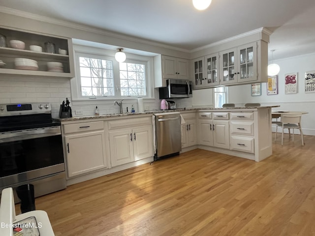 kitchen featuring a sink, appliances with stainless steel finishes, a peninsula, crown molding, and light wood finished floors