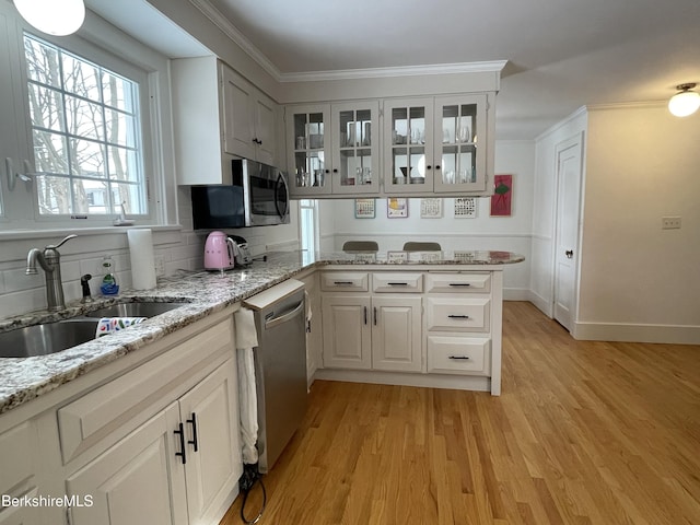 kitchen featuring sink, light stone counters, appliances with stainless steel finishes, light hardwood / wood-style floors, and white cabinets