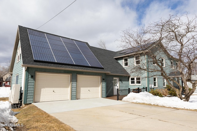 view of front facade featuring a garage, roof mounted solar panels, roof with shingles, and driveway