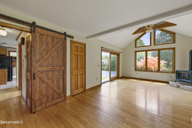 unfurnished living room with ceiling fan, a barn door, light wood-type flooring, and baseboards