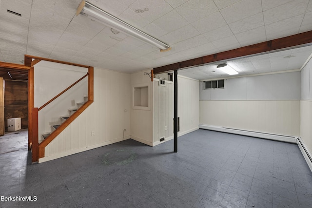 finished below grade area featuring dark floors, stairway, baseboards, wood walls, and baseboard heating