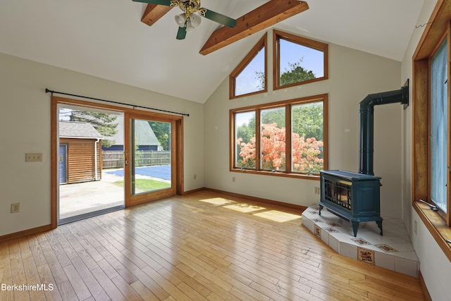 unfurnished living room with a wood stove, beam ceiling, light wood-style floors, a ceiling fan, and high vaulted ceiling