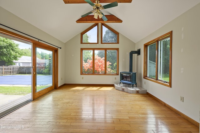 unfurnished living room with a wood stove, light wood finished floors, ceiling fan, and baseboards