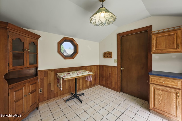 dining space with wainscoting, lofted ceiling, wooden walls, and light tile patterned flooring