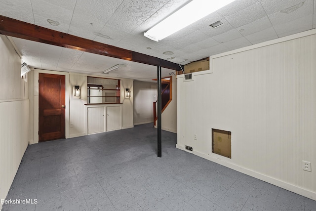 finished basement with tile patterned floors, baseboards, wooden walls, and stairs