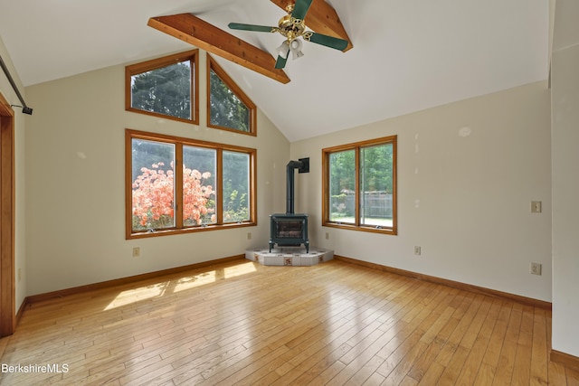 unfurnished living room with a wood stove, light wood-type flooring, beam ceiling, a ceiling fan, and baseboards