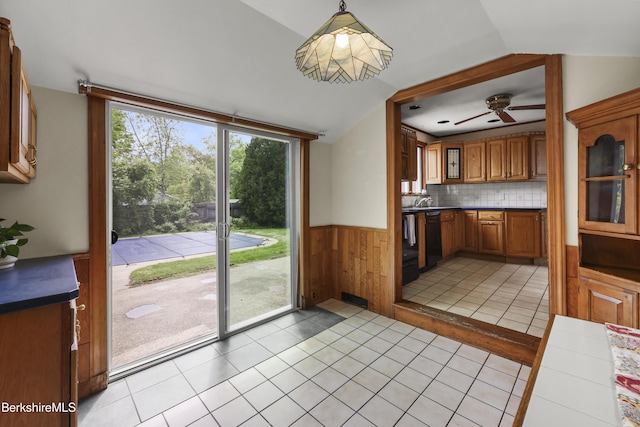 kitchen with black dishwasher, brown cabinetry, wainscoting, vaulted ceiling, and a ceiling fan