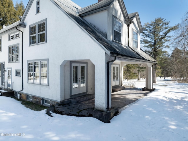 view of snowy exterior with french doors, roof with shingles, and stucco siding