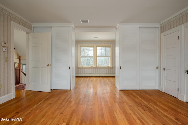 unfurnished bedroom featuring light wood-type flooring, visible vents, two closets, ornamental molding, and wallpapered walls