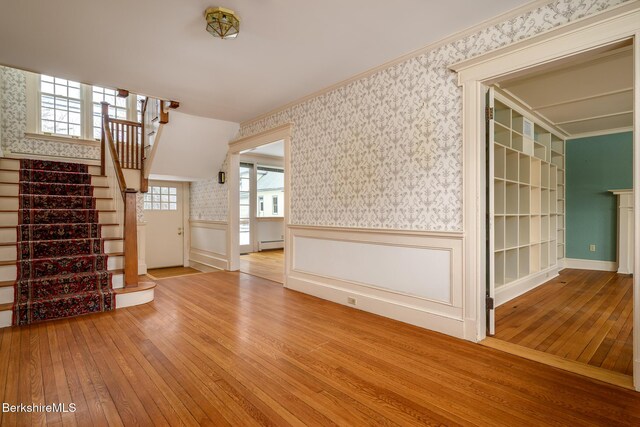 unfurnished living room with wainscoting, wallpapered walls, a baseboard heating unit, and hardwood / wood-style floors