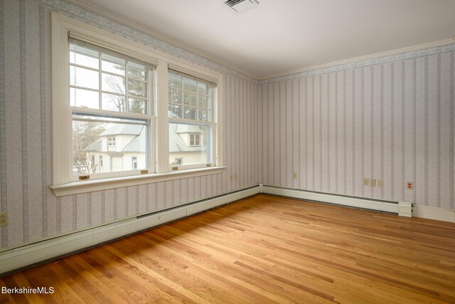 spare room featuring a wealth of natural light, a baseboard heating unit, wood finished floors, and wallpapered walls