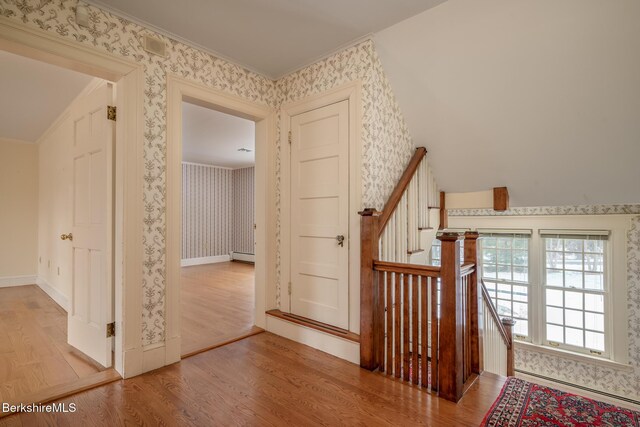 stairs featuring baseboard heating, wallpapered walls, and wood finished floors