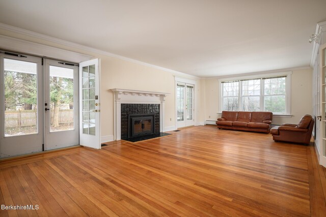 unfurnished living room featuring baseboards, ornamental molding, a tile fireplace, light wood-style floors, and baseboard heating