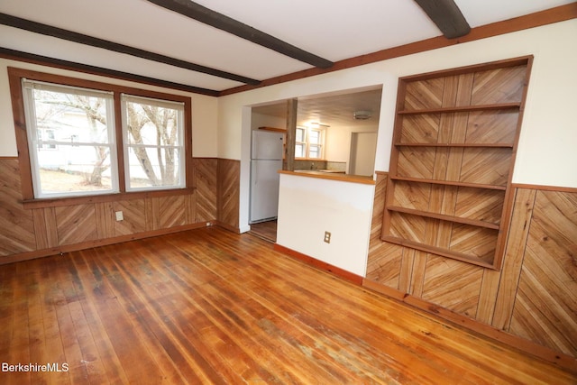 unfurnished living room with beamed ceiling, wooden walls, hardwood / wood-style floors, and wainscoting