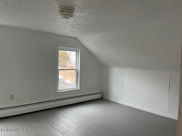 additional living space featuring wood-type flooring, baseboard heating, lofted ceiling, and a textured ceiling