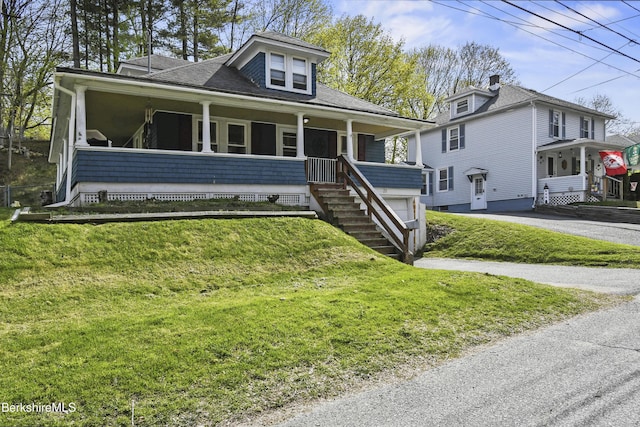 view of front of house with a porch, roof with shingles, driveway, and a front yard