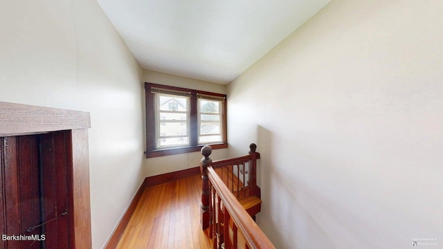 hallway with vaulted ceiling, baseboards, an upstairs landing, and wood finished floors