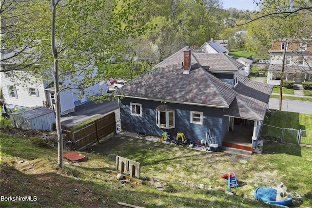 back of house featuring a chimney, roof with shingles, a storage shed, and fence