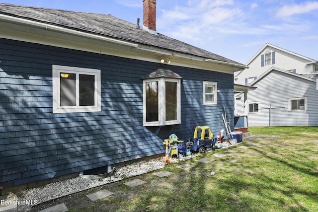 view of side of property with a yard, roof with shingles, and a chimney