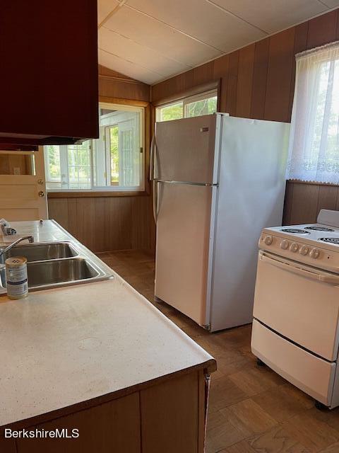 kitchen featuring white appliances, wooden walls, light countertops, a sink, and vaulted ceiling