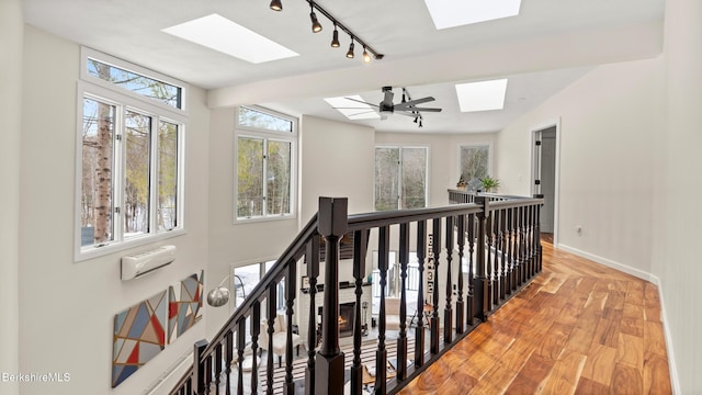 hall featuring a skylight, baseboards, wood finished floors, and an upstairs landing