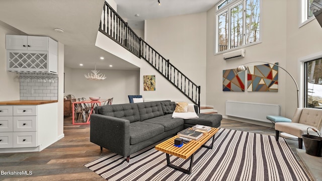 living area with a towering ceiling, radiator heating unit, stairway, dark wood-style flooring, and a wall mounted AC