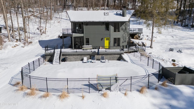 snow covered back of property featuring stairs, a chimney, fence, and a balcony