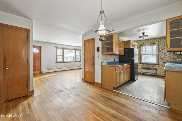 kitchen with radiator heating unit, baseboard heating, pendant lighting, light hardwood / wood-style floors, and black refrigerator