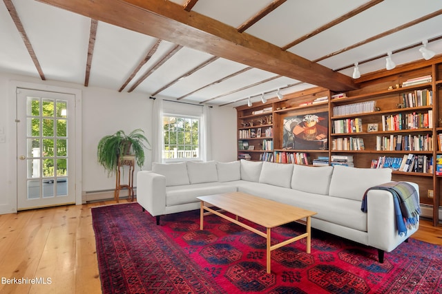 living room featuring rail lighting, baseboard heating, beam ceiling, built in shelves, and light wood-type flooring